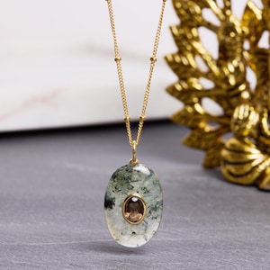 May include: A gold chain necklace with a green and white oval pendant featuring a brown gemstone. The pendant has a unique, natural look.