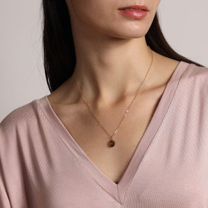 May include: A gold chain necklace with a small, round, brown gemstone pendant.