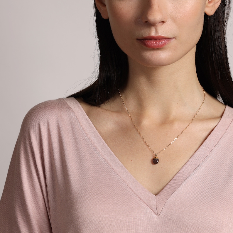 May include: A gold chain necklace with a small, dark purple gemstone pendant.