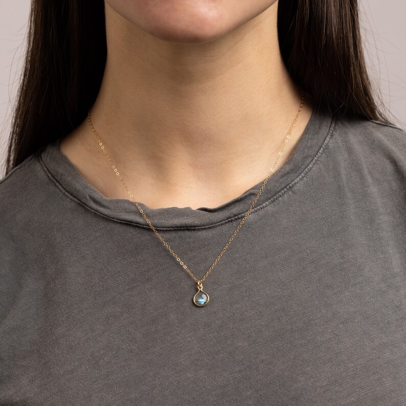 May include: A gold chain necklace with a teardrop-shaped pendant featuring a blue gemstone.