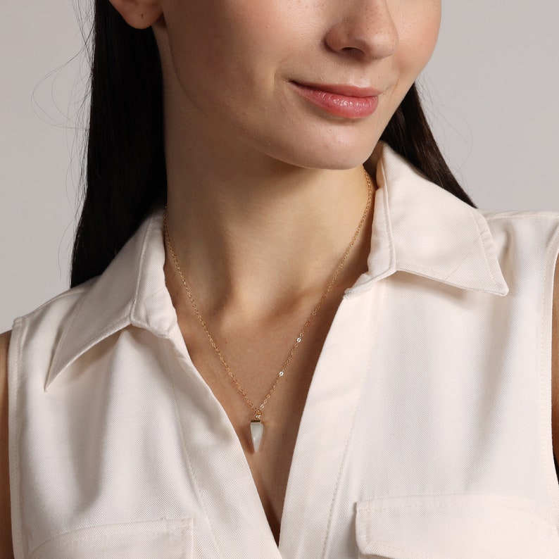 May include: A gold chain necklace with a white triangular pendant.