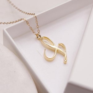 May include: A gold chain necklace with a cursive letter 'S' pendant. The necklace is in a white box.