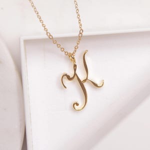 May include: A gold chain necklace with a cursive letter 'K' pendant.