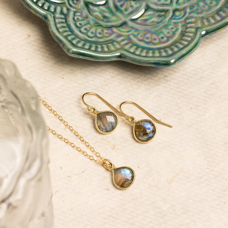 May include: A gold necklace and earrings set with teardrop-shaped labradorite stones. The stones have a iridescent blue and green sheen.