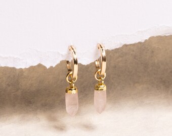 May include: A pair of gold hoop earrings with a pink crystal charm hanging from each hoop.
