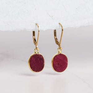May include: A pair of gold dangle earrings with oval-shaped ruby red stones.