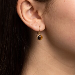 May include: Gold teardrop earrings with a brown tiger's eye gemstone.