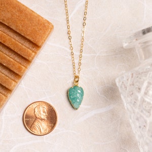 Puede incluir: Un collar de cadena dorada con un colgante de hoja verde tallada. El colgante es aproximadamente del tama&ntilde;o de una moneda de un euro.