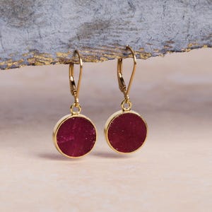 May include: A pair of gold dangle earrings with round, red, textured gemstone accents.