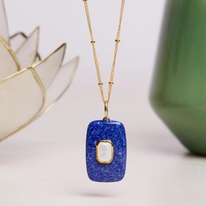 May include: A gold chain necklace with a blue rectangular pendant featuring a white stone in the center.