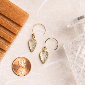May include: A pair of gold earrings with clear leaf-shaped stones hanging from delicate gold hoops.