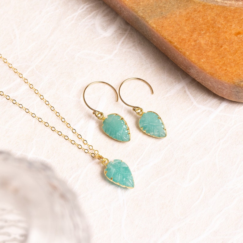Puede incluir: Un conjunto de pendientes y un collar de tono dorado con colgantes de hoja de piedra preciosa verde tallada.