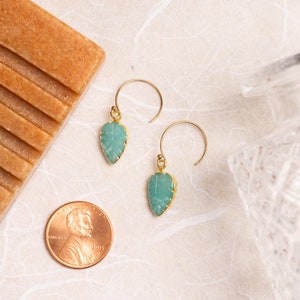 Puede incluir: Un par de pendientes de oro con piedras de color verde turquesa en forma de hoja. Los pendientes cuelgan de un gancho de oro.