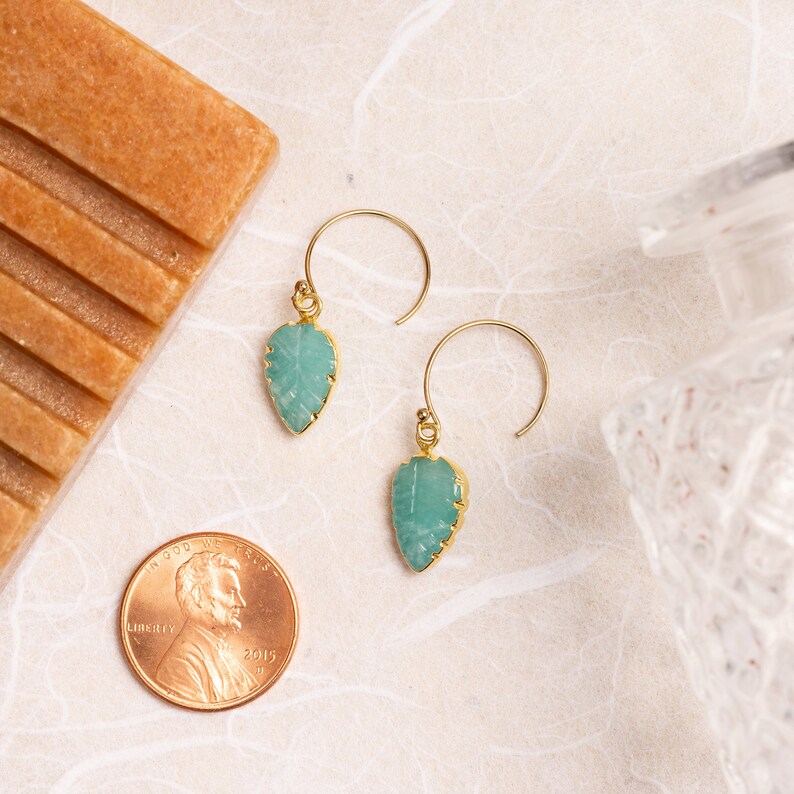Puede incluir: Un par de pendientes de oro con piedras de color verde turquesa en forma de hoja. Los pendientes cuelgan de un gancho de oro.