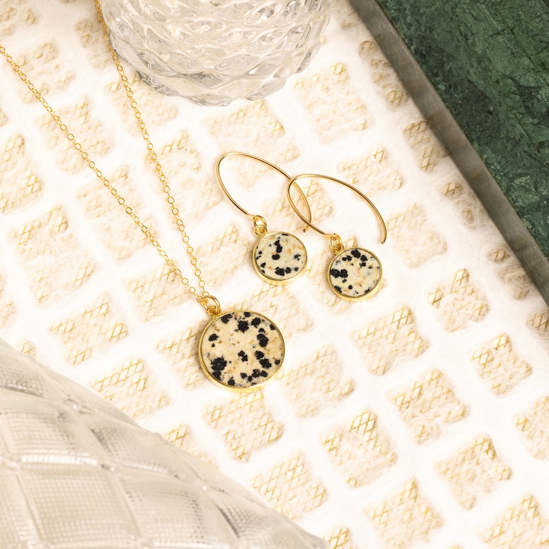 May include: A gold necklace and earrings set with a round dalmatian jasper pendant and matching earrings.