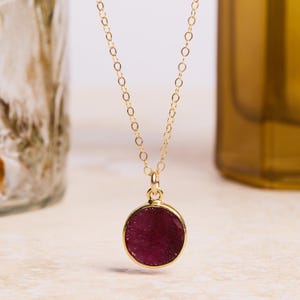 May include: A gold chain necklace with a round, dark red gemstone pendant.