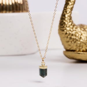 May include: A gold chain necklace with a dark green gemstone pendant. The pendant is shaped like a point and has a gold trim.