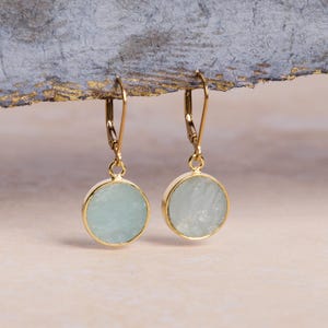 May include: Gold earrings with light blue round aquamarine stones.