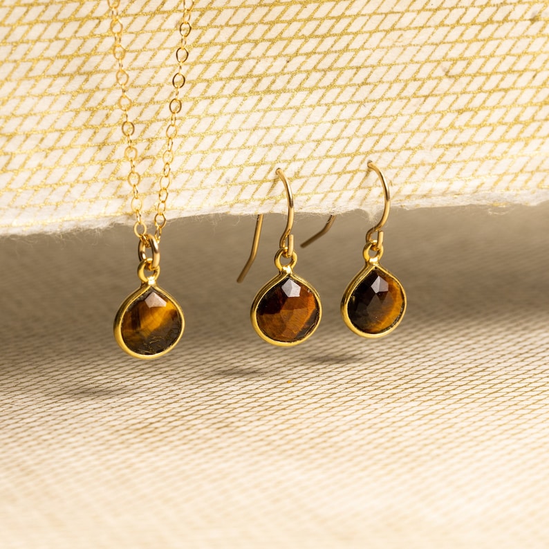 May include: A gold necklace and earrings set with teardrop-shaped tiger's eye stones.