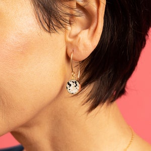 May include: Gold hoop earrings with a round dalmatian jasper stone pendant.
