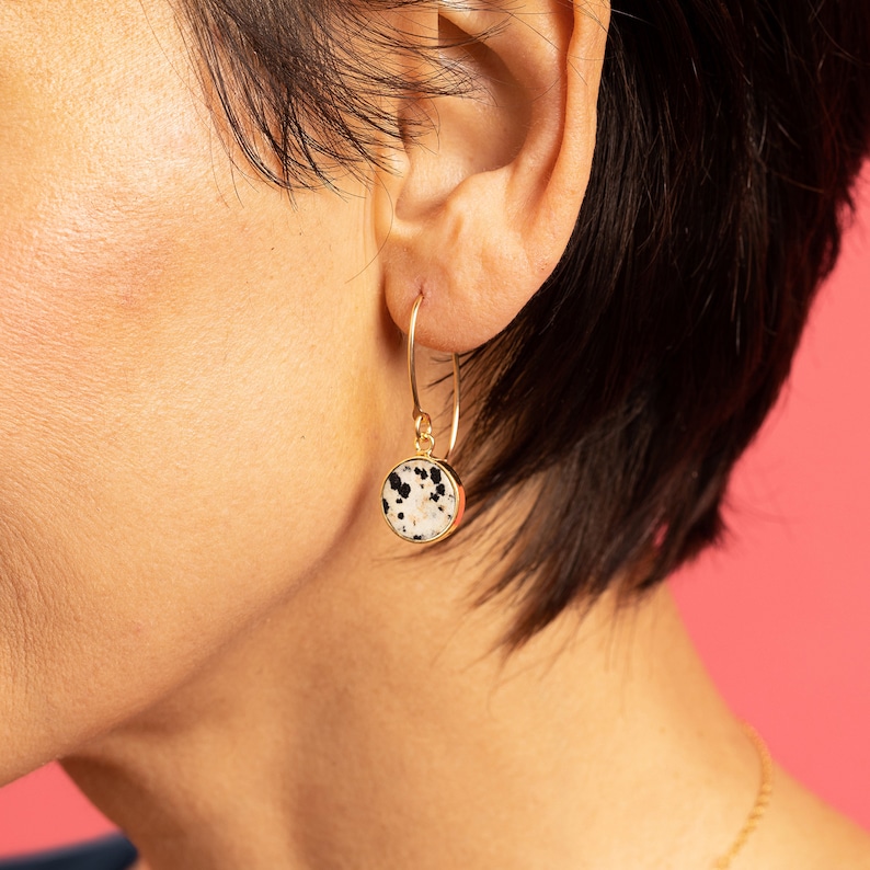 May include: Gold hoop earrings with a round dalmatian jasper stone pendant.