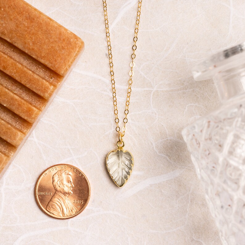 May include: A gold chain necklace featuring a clear, faceted leaf pendant. The pendant is heart-shaped and has a delicate, intricate design.