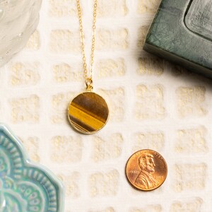 May include: Gold necklace with a round tiger's eye pendant. The pendant is about the size of a US penny.