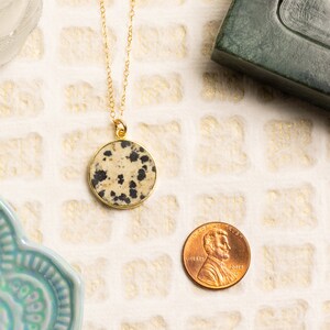 May include: Gold chain necklace with a round dalmatian jasper pendant. The pendant is about the size of a US penny.