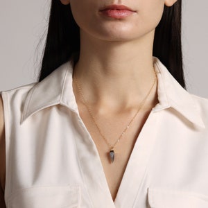 May include: A gold chain necklace with a grey, pointed pendant.