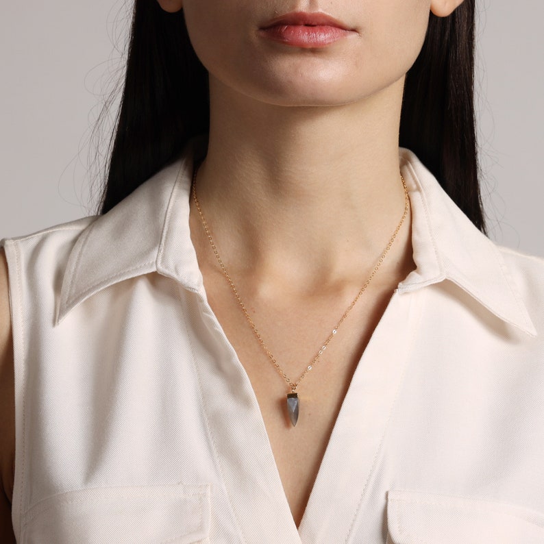 May include: A gold chain necklace with a grey, pointed pendant.