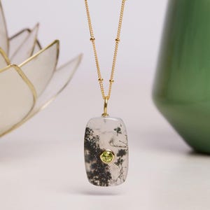 May include: A gold chain necklace with a rectangular pendant featuring a white agate stone with black dendritic inclusions and a small green gemstone in the center.