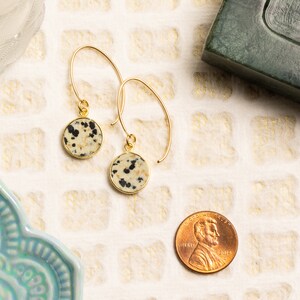 May include: A pair of gold dangle earrings with round dalmatian jasper stone accents. The earrings are approximately the size of a US penny.