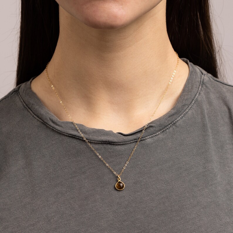 May include: A gold chain necklace with a small, teardrop-shaped brown gemstone pendant.