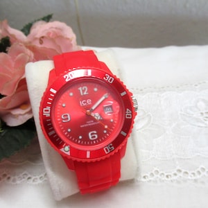 May include: A bright red analogue wristwatch with a silicone strap and a matching red dial. The watch face features white Arabic numerals at the 6, 9, and 12 o'clock positions, a date window at 3 o'clock, and the word ice printed in white.