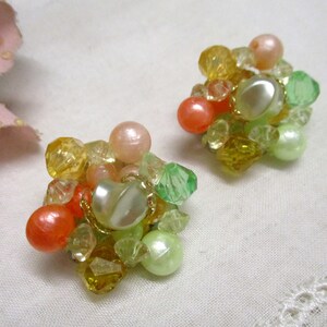 Może przedstawiać: Para klips&oacute;w z gromadą pastelowych zielonych, ż&oacute;łtych i pomarańczowych koralik&oacute;w.