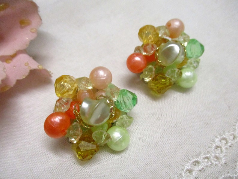 Może przedstawiać: Para klips&oacute;w z gromadą pastelowych zielonych, ż&oacute;łtych i pomarańczowych koralik&oacute;w.