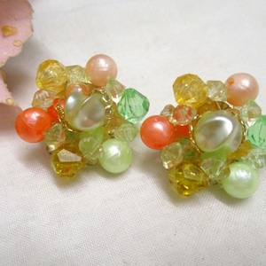 Może przedstawiać: Para vintage'owych kolczyk&oacute;w na klipsie z gromadą pastelowych zielonych, ż&oacute;łtych, pomarańczowych i białych koralik&oacute;w.