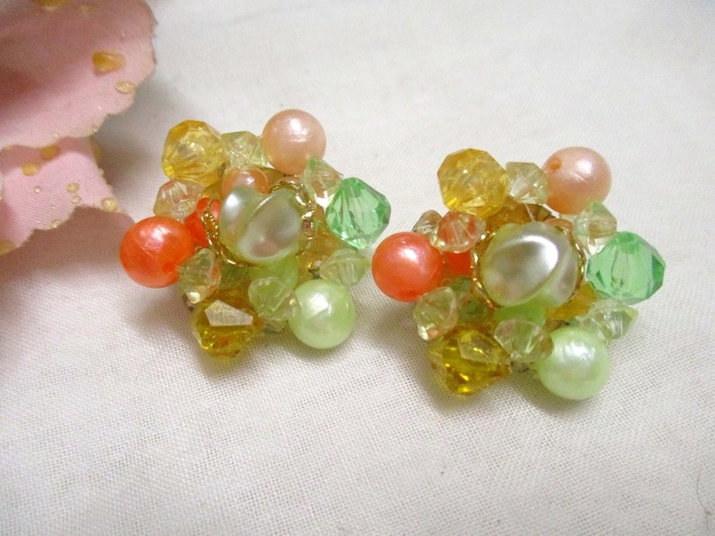 Może przedstawiać: Para vintage'owych kolczyk&oacute;w na klipsie z gromadą pastelowych zielonych, ż&oacute;łtych, pomarańczowych i białych koralik&oacute;w.