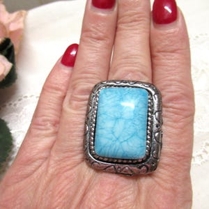 Könnte beinhalten: Ein großer, rechteckiger Ring mit einem hellblauen Stein in einem silberfarbenen Metallrahmen. Der Stein hat ein marmoriertes Aussehen. Der Ring ist ein auffälliges Schmuckstück, das jedem Outfit einen Farbtupfer verleiht.
