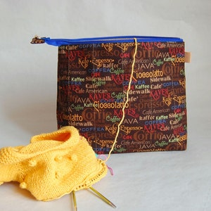 May include: A brown zippered pouch with a coffee-themed print. The pouch is filled with yellow yarn and knitting needles. The print includes the words "Cafe American", "Kaffee", "Java", "Espresso", "Sidewalk", "Coffee", and "Kaves".