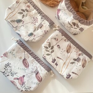 May include: Four fabric project bags with a floral pattern in shades of pink, green, and brown on a white background. The bags have a drawstring closure and a gray trim. One bag is open and filled with yarn.