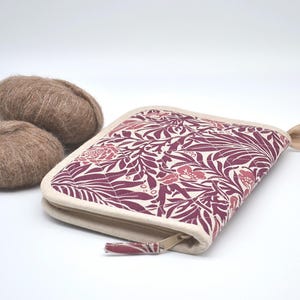 Puede incluir: Un estuche con cremallera con un estampado floral en burdeos y crema, junto a dos ovillos de lana marr&oacute;n. El estuche tiene un borde color crema y una leng&uuml;eta a juego. La lana parece suave y esponjosa.