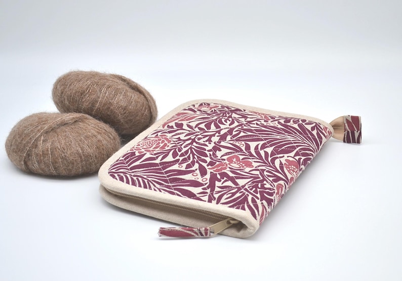 Puede incluir: Un estuche con cremallera con un estampado floral en burdeos y crema, junto a dos ovillos de lana marr&oacute;n. El estuche tiene un borde color crema y una leng&uuml;eta a juego. La lana parece suave y esponjosa.