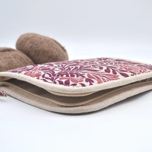 Puede incluir: Un estuche con cremallera con un estampado floral en tonos rosa y burdeos, con un borde beige. Dos ovillos de lana marr&oacute;n est&aacute;n detr&aacute;s del estuche. El estuche tiene una cremallera beige y un tirador estampado.