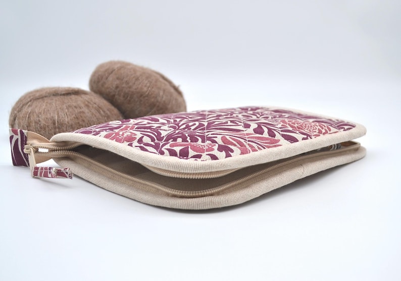 Puede incluir: Un estuche con cremallera con un estampado floral en tonos rosa y burdeos, con un borde beige. Dos ovillos de lana marr&oacute;n est&aacute;n detr&aacute;s del estuche. El estuche tiene una cremallera beige y un tirador estampado.