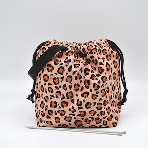 Puede incluir: Una bolsa de cordón de color rosa y naranja con estampado de leopardo, con una correa negra y dos agujas de tejer plateadas.