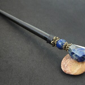 May include: Black wooden hair stick with a blue and silver gemstone and a decorative metal accent.