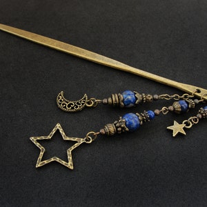 Puede incluir: Una varita para el pelo dorada con un encanto de media luna y estrella, acentuada con cuentas de lapisl&aacute;zuli azul y una cadena.