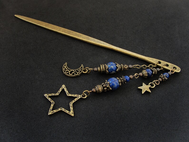 Puede incluir: Una varita para el pelo dorada con un encanto de media luna y estrella, acentuada con cuentas de lapisl&aacute;zuli azul y una cadena.