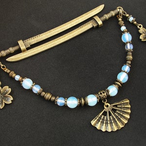 Op de afbeelding: Een bronzen haarspeld met een zwaardontwerp en een kralenketting met opaalachtige kralen, een waaierbedel en twee bloembedels.